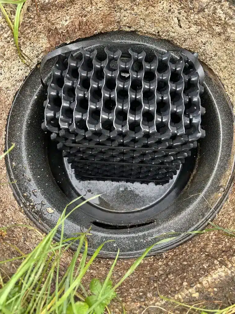 Bloc de drainage alvéolé noir installé dans un regard circulaire au sol.
